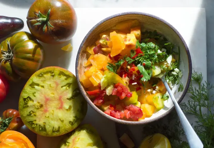 En skål med färgglad pico de gallo, omgiven av olika sorters tomater.