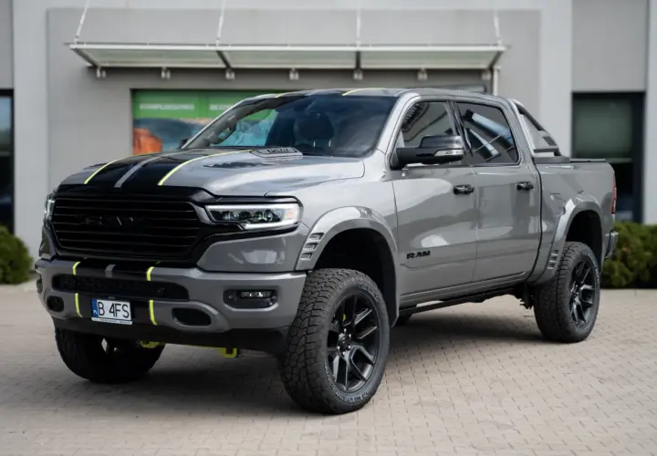 Szary Dodge Ram 1500 z żółtymi akcentami i czarnymi pasami na masce, zaparkowany przed budynkiem.