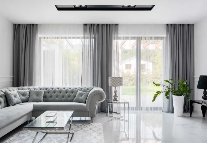 Eleganckie aranżacje okna w salonie: szara sofa, szklane stoliki i zasłony tworzą przytulną atmosferę.