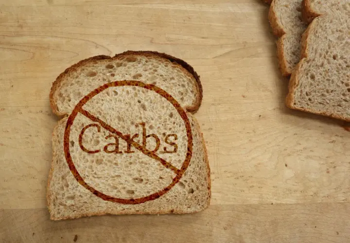 Kromka chleba z przekreślonym napisem "Carbs". Idealne dla osób szukających produktów bez węglowodanów, tabela z nimi może być pomocna.