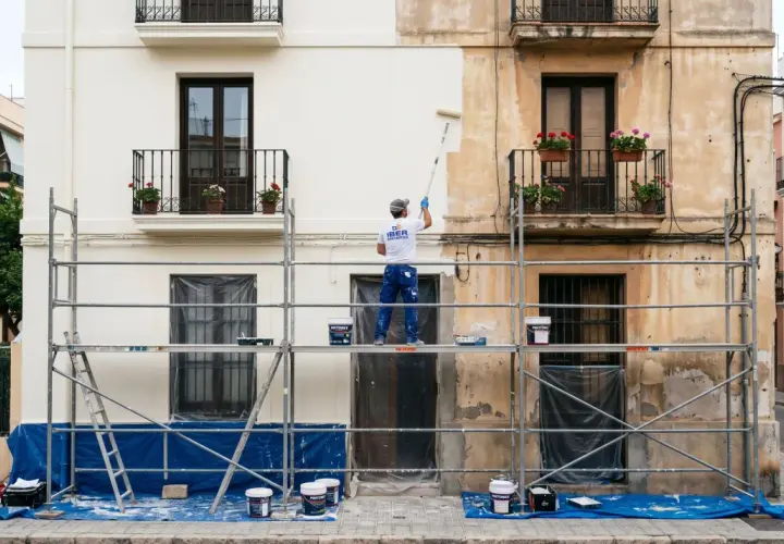 Un pintor en andamios renueva la fachada de un edificio, listo para pintar casa exterior.