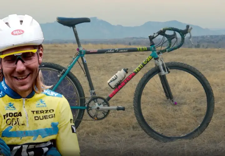 A smiling cyclist in a yellow jersey stands beside a vintage YETI C-26 bike, hinting at where YETI bikes are made.