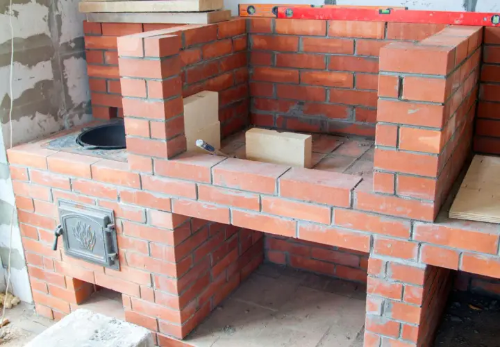 Construction d'un barbecue fait maison en briques rouges. Des briques supplémentaires et un niveau à bulle sont visibles sur le chantier.