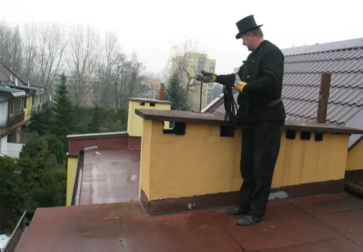 Kominiarz w cylindrze na dachu z liną. Czy kominiarz może dać mandat za zaniedbany komin?