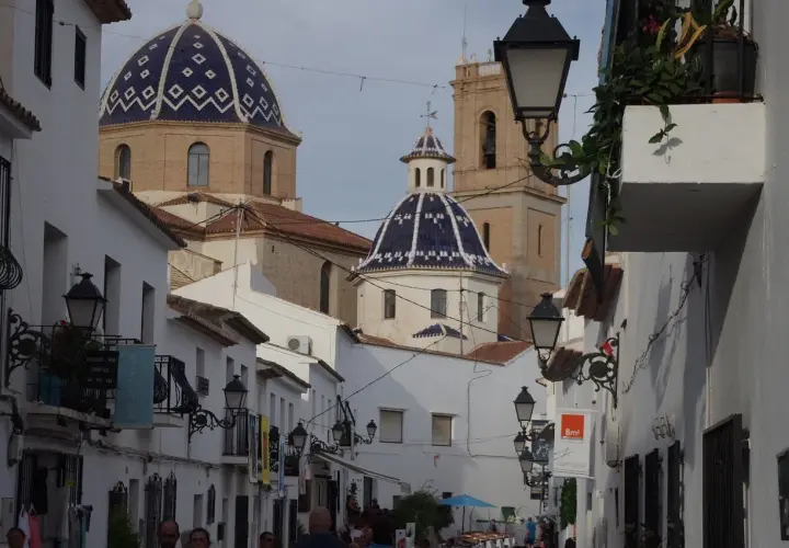 Calle estrecha con casas blancas y cúpulas azules, un ejemplo de los pueblos más bonitos de Alicante.