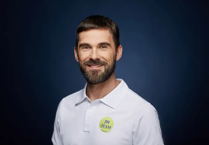 Paweł Habrat, uśmiechnięty mężczyzna z brodą, w białej koszulce polo z logo "JW TEAM".