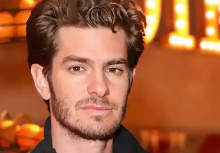Andrew Garfield, avec une barbe naissante, pose devant des lumières chaudes. On spécule sur son prochain film.