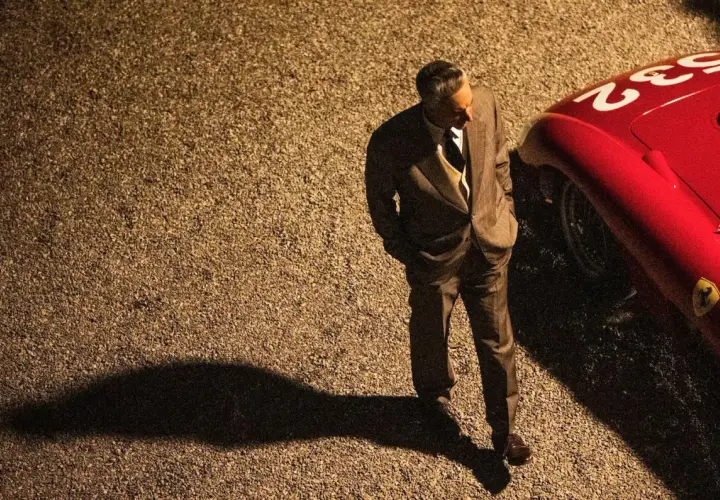 Mężczyzna w garniturze stoi obok czerwonego Ferrari. Zapowiedź filmu "Ferrari" budzi emocje, jak te wyścigi.