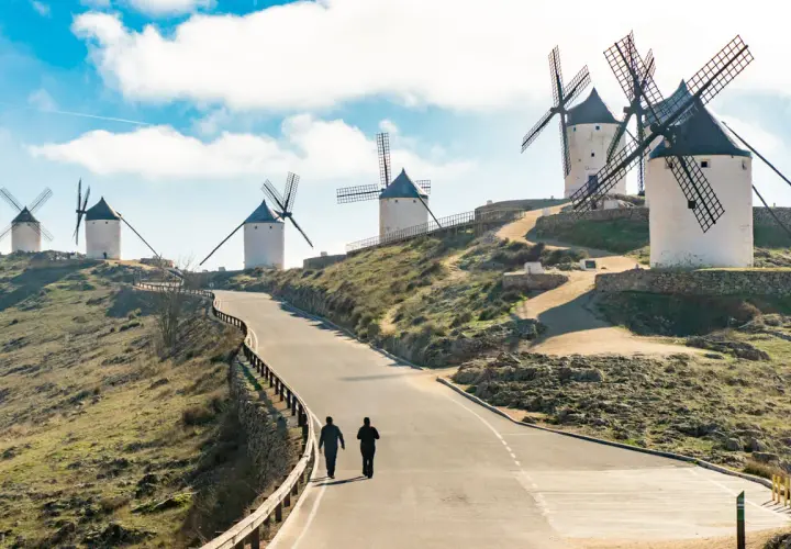 Molinos de viento en la ruta de Don Quijote, con dos personas caminando por un camino.