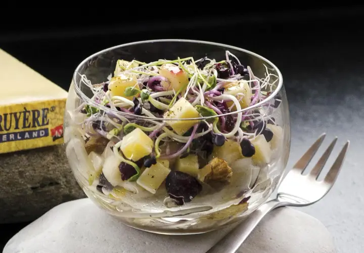 Deliciosa ensalada de endivias con trozos de queso Gruyère, arándanos y brotes frescos, servida en copa de cristal.