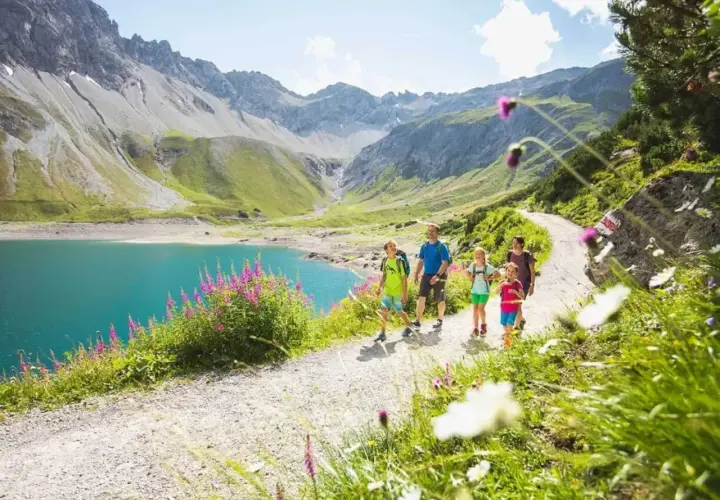 Familie genießt eine Wanderung im Brandnertal. Türkiser Bergsee, grüne Hänge und blühende Wiesen.