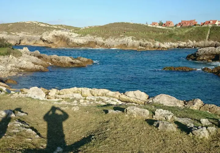 La **playa de Canallave** se asoma entre rocas y aguas turquesas. En la colina, casas de tejados rojos vigilan el mar.