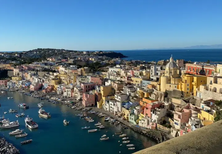 Vue panoramique de Procida ou Ischia, avec ses maisons colorées nichées sur la côte et des bateaux dans le port.