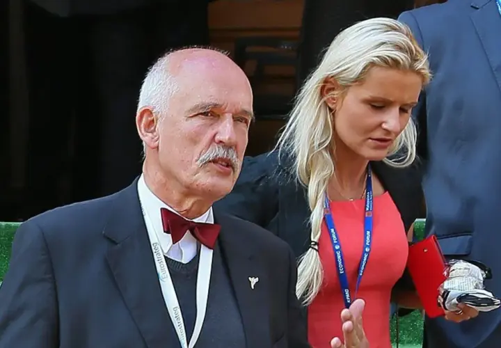 Janusz Korwin-Mikke z wąsem i w muszce, obok niego kobieta w czerwonej sukience. Może to jego dzieci?