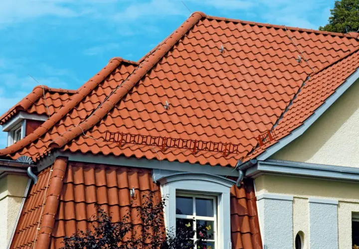 Dwa rodzaje dachów z czerwonej dachówki ceramicznej, jeden płaski, drugi skośny, pod błękitnym niebem.