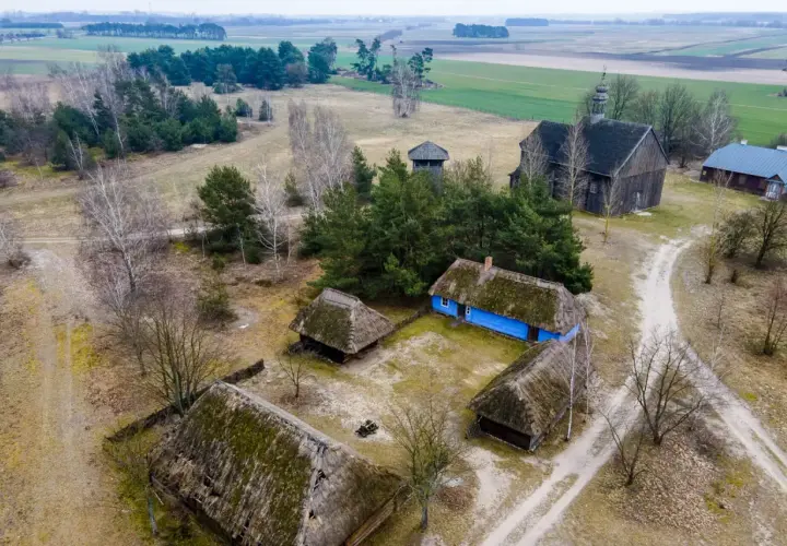 Skansen wsi łowickiej z drewnianymi chatami, kościołem i wieżą.