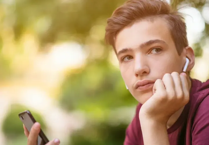 Chłopak z telefonem i słuchawkami zastanawia się, o czym rozmawiać z dziewczyną przez telefon.
