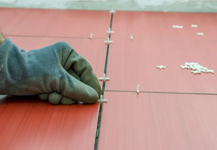 Main tenant, ganté, ajuste des croisillons pour refaire le joint du carrelage rouge.