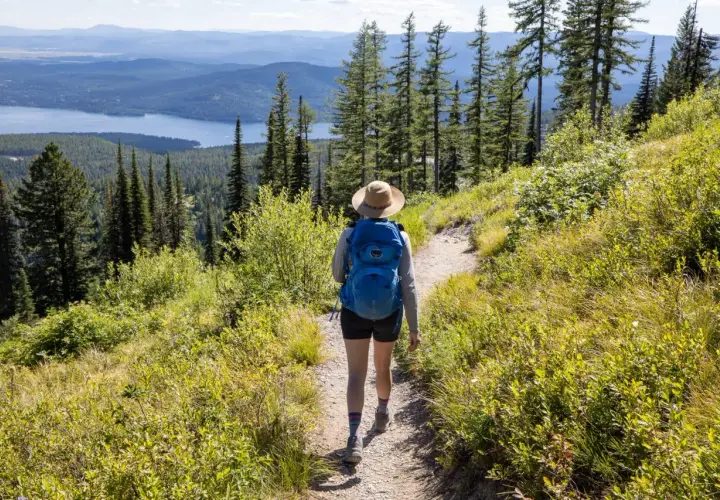 A hiker with a blue backpack walks on a trail, enjoying one of the best long hikes in the world with a stunning lake and mountain view.
