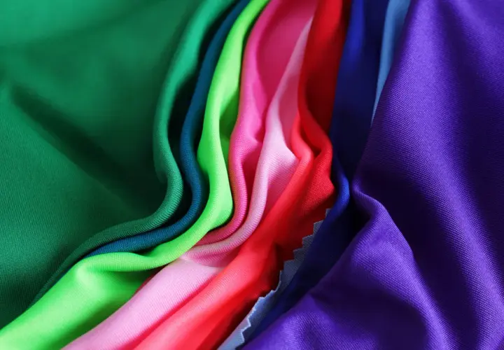 A vibrant collection of athletic wear fabric swatches in green, teal, lime, pink, red, blue, and purple, draped and folded.