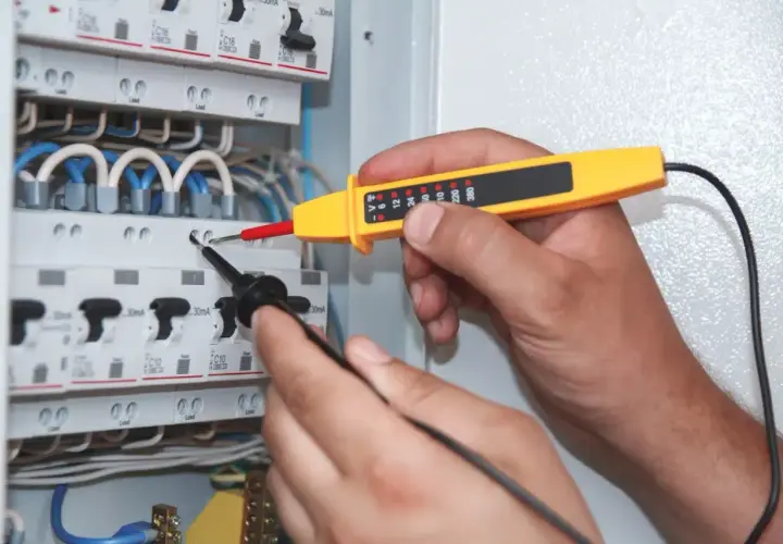 Elektryk sprawdza napięcie w skrzynce bezpieczników. Miernik wskazuje moc pozorną, pomagając zapewnić bezpieczeństwo instalacji.