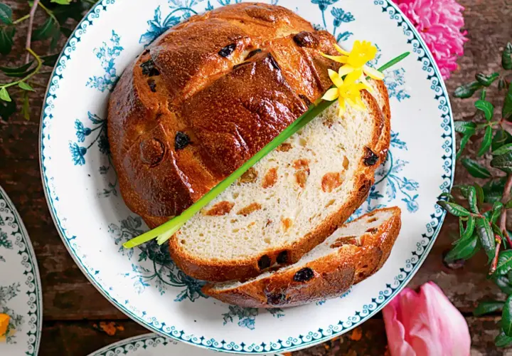 Pan di ramerino dorato, con uvetta e scorze candite, guarnito con un fiore giallo e un rametto verde.