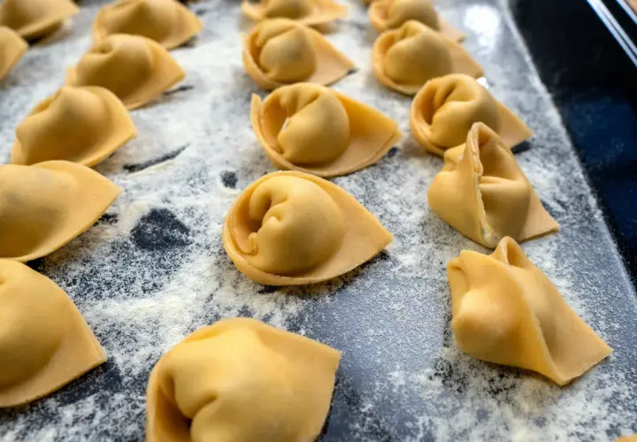 Frisch geformte Tortellini liegen auf einer bemehlten Fläche. Das Selbermachen von Tortellini ist ein Genuss für alle Sinne.