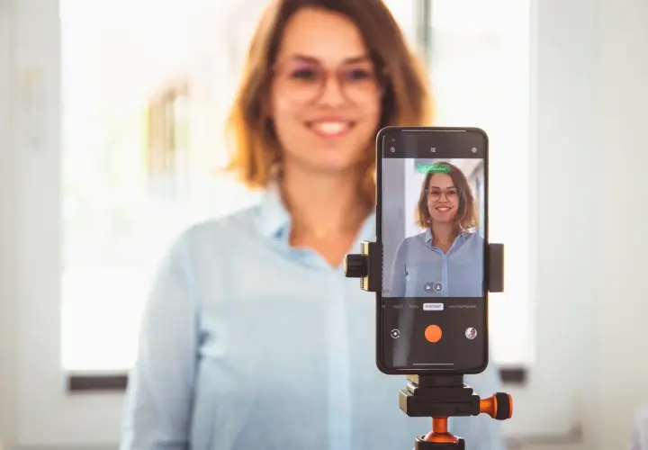 Frau macht ein bewerbungsfoto selber machen mit dem Handy auf einem Stativ.