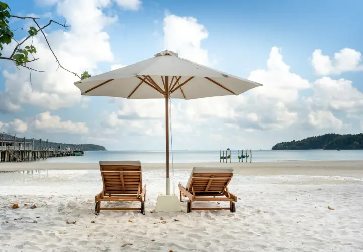 Dwie leżaki pod parasolem na piaszczystej plaży. Idealne miejsce, by odpocząć i zastanowić się, gdzie lecieć w czerwcu.