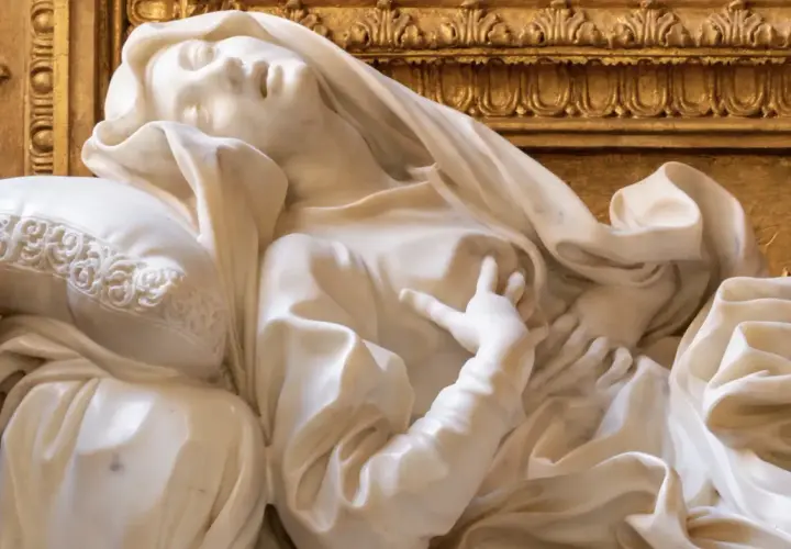 Scultura in marmo di Santa Teresa in estasi, capolavoro barocco a Roma. La sua mano sfiora il petto, mentre il volto esprime un profondo trasporto spirituale.