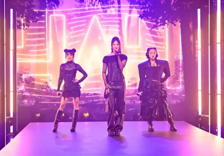 Trzy artystki k-pop w czarnych, stylizowanych strojach na scenie z neonowym tłem.