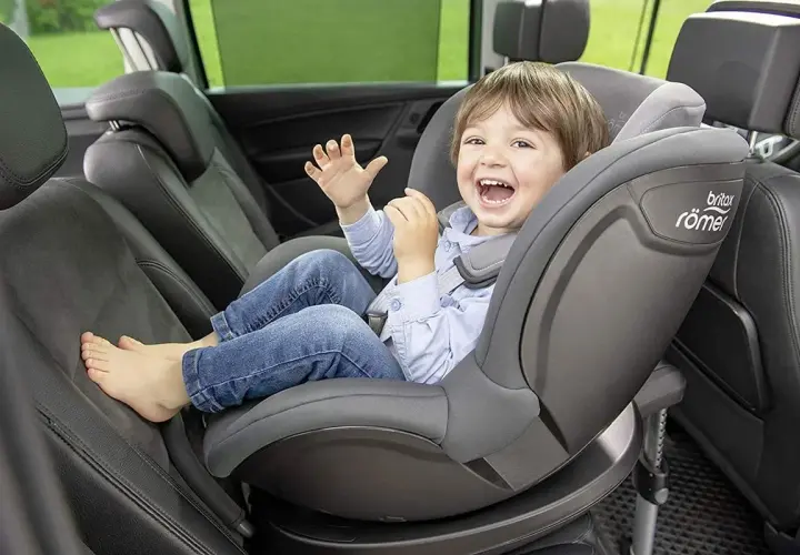 Uśmiechnięty chłopiec w foteliku samochodowym Britax Römer.