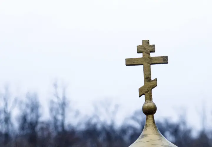 Złoty krzyż prawosławny na tle pochmurnego nieba. Symbolizuje nadzieję i pamięć podczas pogrzebu prawosławnego.