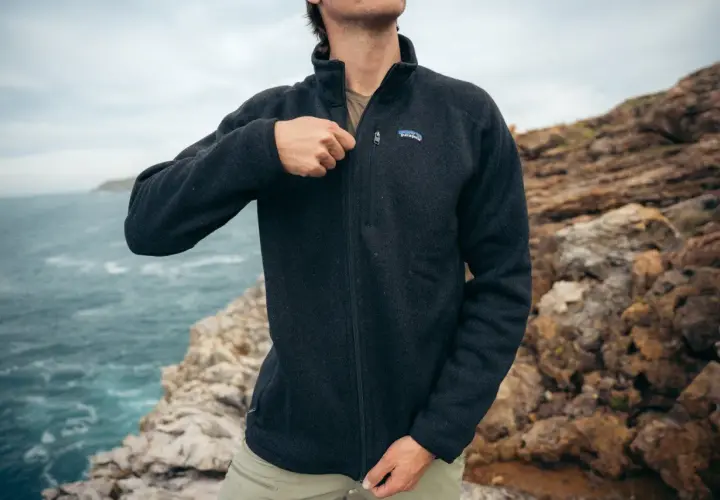 A man zips up a dark grey sweater fleece jacket, perfect for a coastal adventure. The textured fabric offers warmth and comfort.