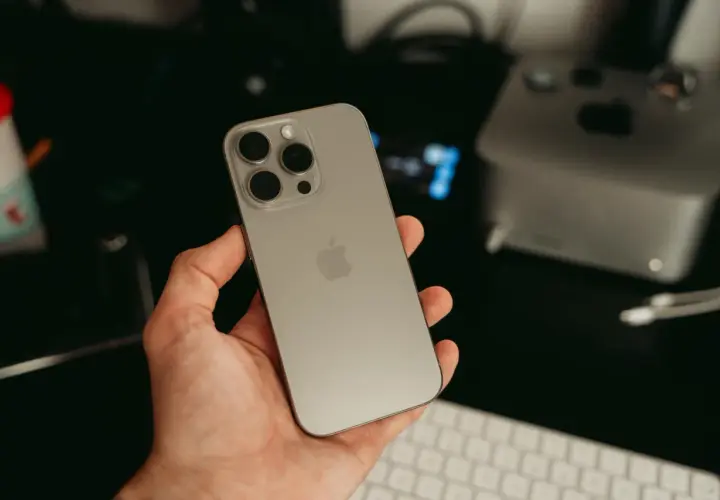 Dłoń trzyma nowy iPhone 16 ultramaryna. Z tyłu widoczny moduł aparatów i logo Apple.