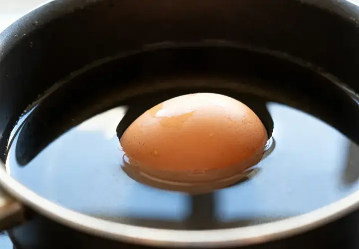 Un œuf frais flotte dans l'eau d'une casserole, prêt à être cuit.