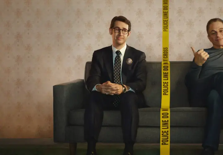 Dwóch mężczyzn siedzi na kanapie. Jeden, ubrany w garnitur, to **the good cop**. Obok niego, za taśmą policyjną, drugi mężczyzna uśmiecha się.