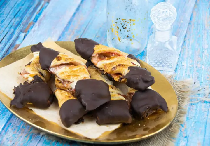 Deliciosos lazos de hojaldre con relleno de fresa, bañados en chocolate negro. Un dulce tentempié perfecto.