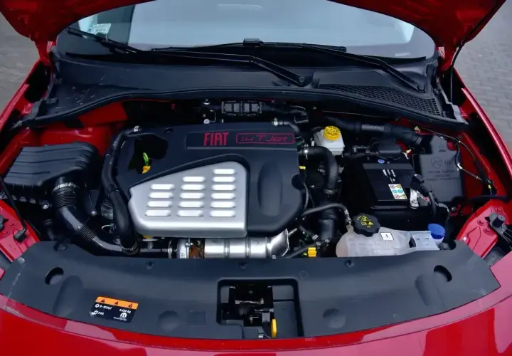 Silnik fiat bravo 1.4 t-jet w komorze pod maską. Widoczny akumulator, układ dolotowy i osłona silnika.