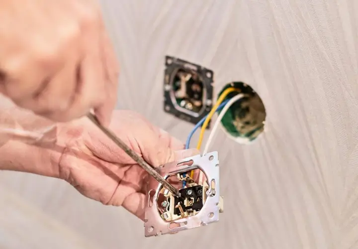 Instalator podłącza włącznik światła podwójny trzy przewody. Widać rękę z wkrętakiem i mechanizm włącznika.