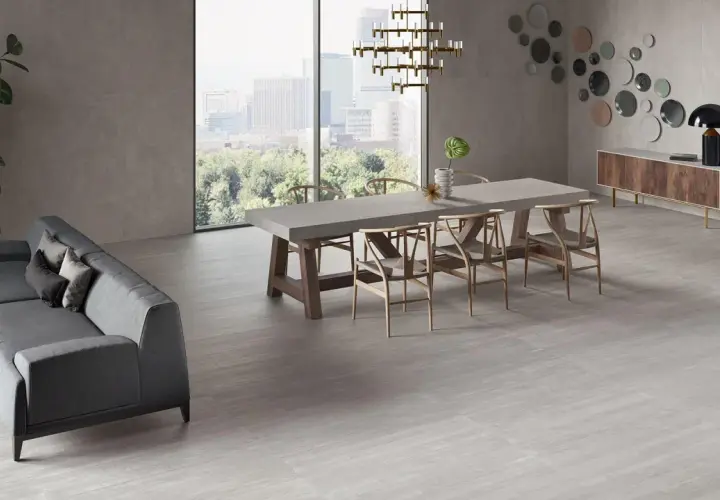 Un elegante soggiorno con divano grigio, tavolo da pranzo in cemento e sedie in legno, il tutto su un pavimento in gres porcellanato ruvido che evoca un'atmosfera moderna e accogliente.