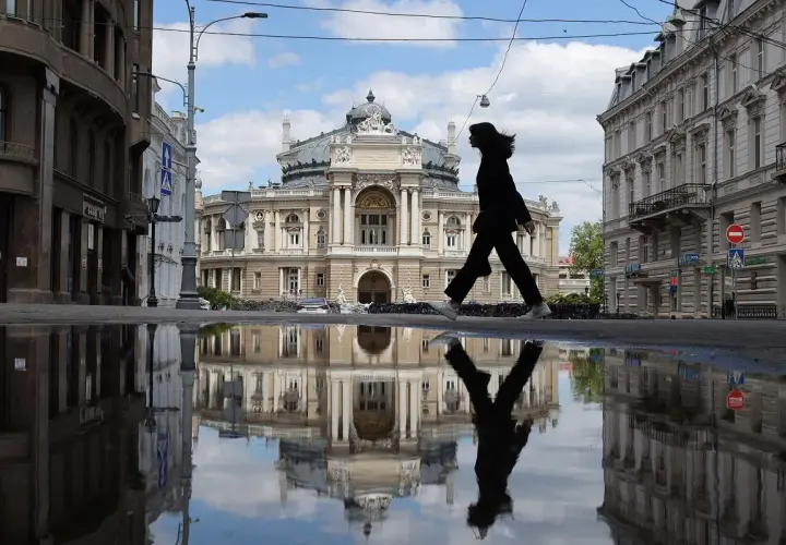 Kobieta idzie przez kałużę przed Teatrem Opery i Baletu w Odessie, tworząc odbicie niczym z filmu.