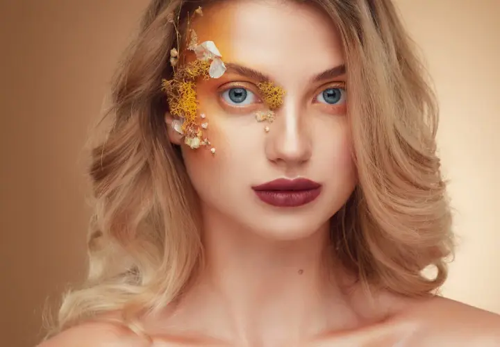 Fotografia beauty: blondynka z niebieskimi oczami, makijażem inspirowanym naturą i ozdobami z suszonych kwiatów na twarzy.