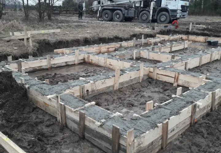 Rozpoczęła się budowa domu drewnianego. Wylano fundamenty, widać drewniane szalunki i świeży beton. W tle stoi gruszka z betonem.