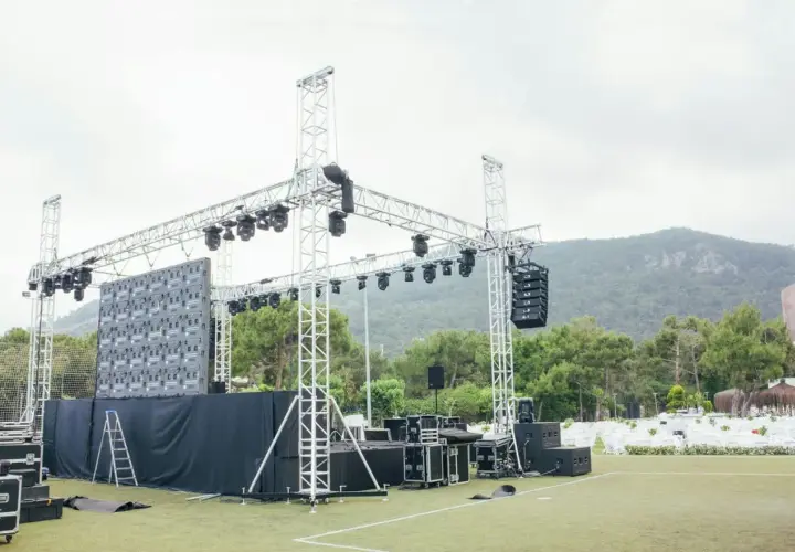 Scena z ekranem LED i różnymi rodzajami oświetlenia scenicznego, głośnikami i konstrukcjami aluminiowymi, gotowa na wydarzenie.