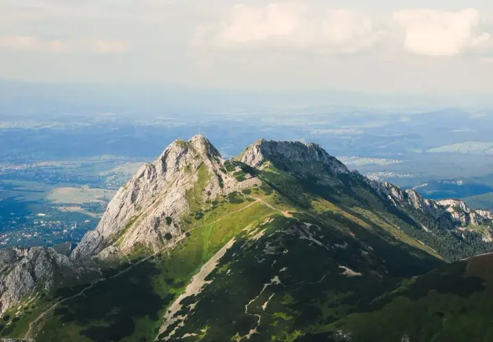 Górskie szczyty z zielonymi zboczami i kamienistymi graniami, w oddali widać dolinę i chmury.