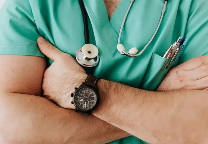 Medico con camice verde, stetoscopio e orologio, pronto ad ascoltare. La sua espressione suggerisce un'attenta valutazione, forse in vista di una **denuncia medico di base**.