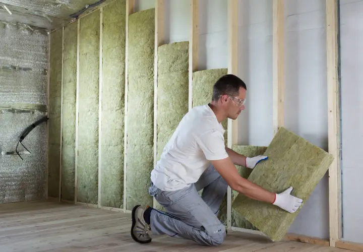 Un ouvrier installe un panneau d'isolant thermique dans une structure murale en bois.