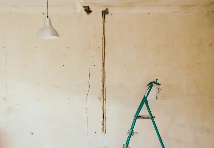 Pękające ściany starego domu, widoczna instalacja elektryczna i drabina.