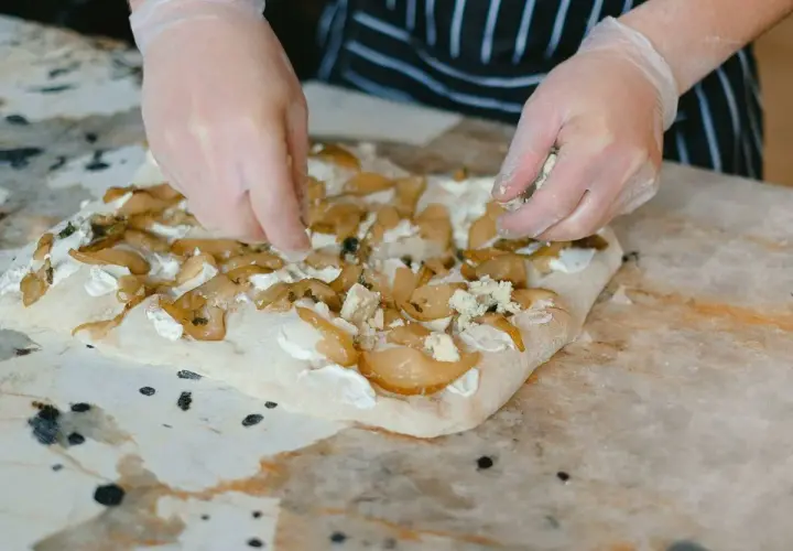 Manos enguantadas añaden queso azul a una focaccia con peras. Una deliciosa focaccia reteta en proceso.